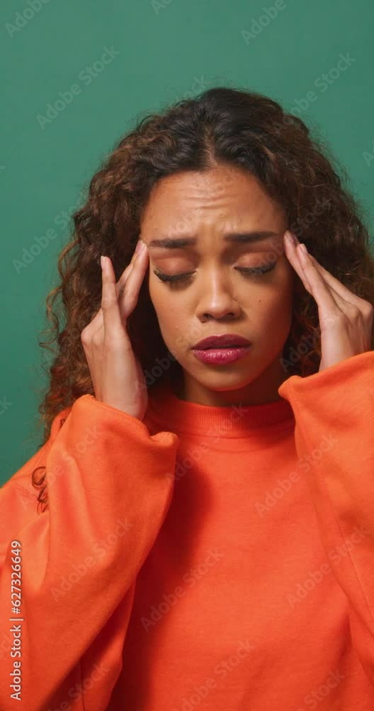 Young multi-ethnic woman rubs temples, headache, green studio background Young multi-ethnic woman rubs temples, headache, green studio background