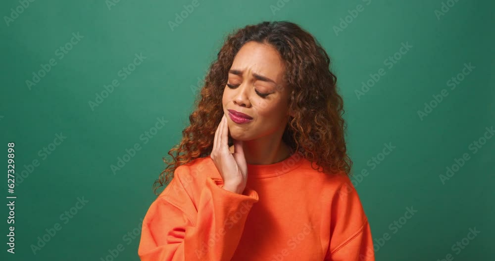 Young biracial woman rubs jaw in pain, toothache, studio green background orange Young biracial woman rubs jaw in pain, toothache, studio green background orange