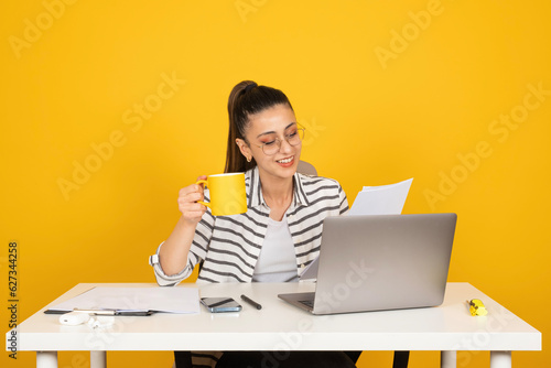 Business woman working, young caucasian brunette business woman working. Holding coffee mug and papers checking accounts from laptop. Sit work at white office desk. Achievement career concept idea. photo