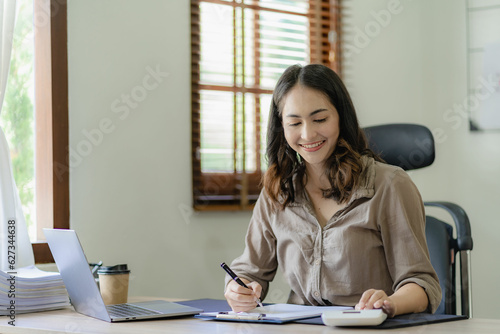 Asian woman working on documents on laptop at work sitting at desk planning financial report business plan investment Financial business analysis and research concepts.
