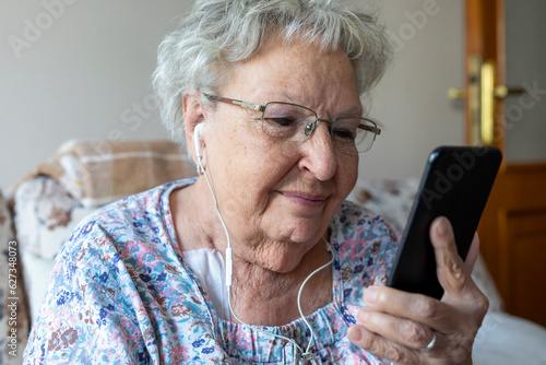 Happy elderly woman enjoying using mobile apps,  smiling senior woman holding smartphone, looking at mobile phone screen, browsing social media at home