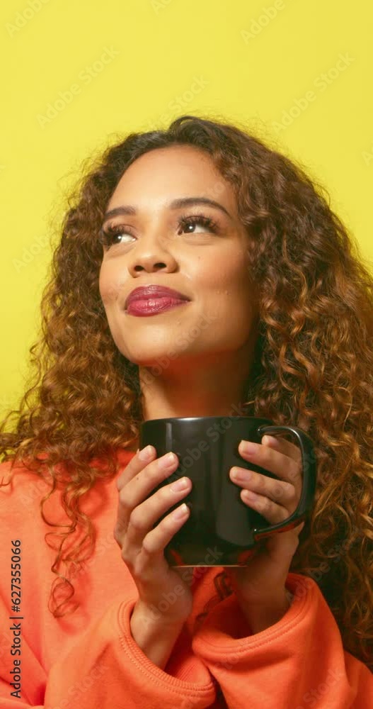 Contented biracial woman sips warm drink from mug, yellow studio background Contented biracial woman sips warm drink from mug, yellow studio background