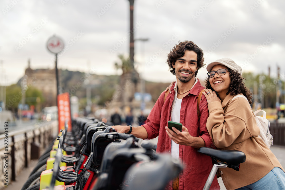 A cheerful couple with mobile phone is renting the bikes while smiling at the camera.