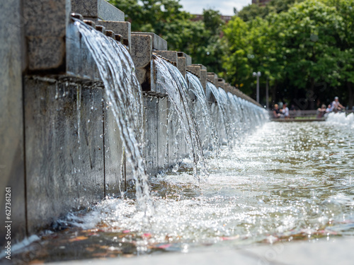 Water flows over the stone slabs of the city fountain. Fountain in the city park.