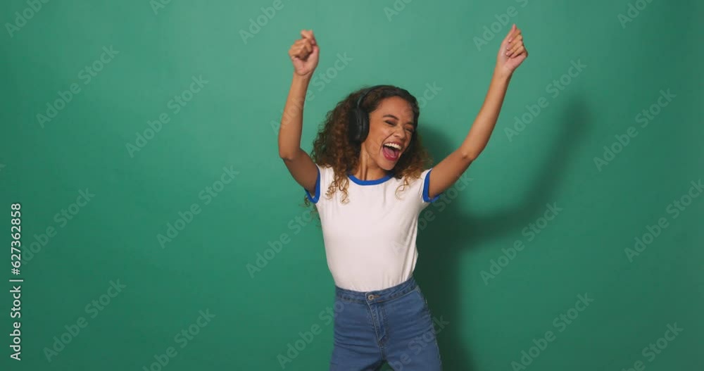 Wide shot, young biracial woman dancing with headphones, green studio background Wide shot, young biracial woman dancing with headphones, green studio background