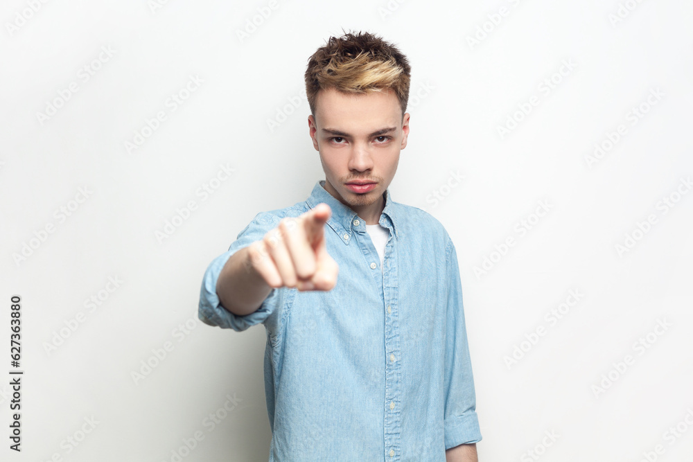 Portrait of bossy strict man wearing denim shirt looking and indicating to camera, choosing you, you have problems, has serious expression. Indoor studio shot isolated on gray background. Portrait of bossy strict man wearing denim shirt looking and indicating to camera, choosing you, you have problems, has serious expression. Indoor studio shot isolated on gray background.