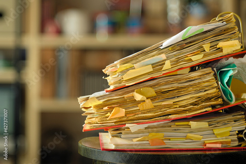 stack of dusty messy file folders with narrow depth of field, blurred office in the back,red tape, bureaucracy,aministration,business concept. photo