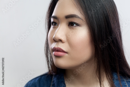 Closeup portrait of pensive thoughtful attractive young adult brunette woman with beautiful makeup and long hair, looking away. Indoor studio shot isolated on gray background.
