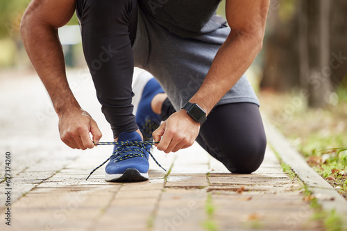 Man, hands and tying shoe in park for running, fitness or cardio workout and exercise in the outdoors. Hand of male person, runner or athlete tie shoes and getting ready for sports training in nature