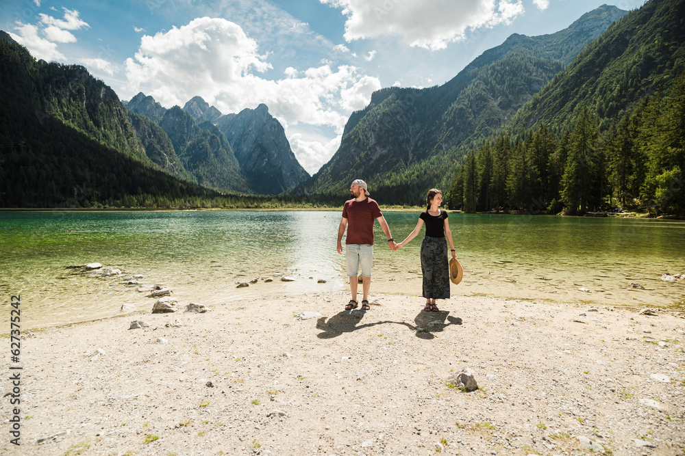 Beautiful traveler couple in front of the iconic and stunning Lago di Dobbiaco, The Dolomites, Italy