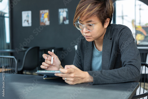 Step into the modern world of digital creativity with a young, smart Asian woman as she navigates her online workplace for her freelance work, using applications, touchpad, and wireless communication.