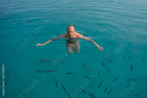 a man swims in a turquoise sea full of fish