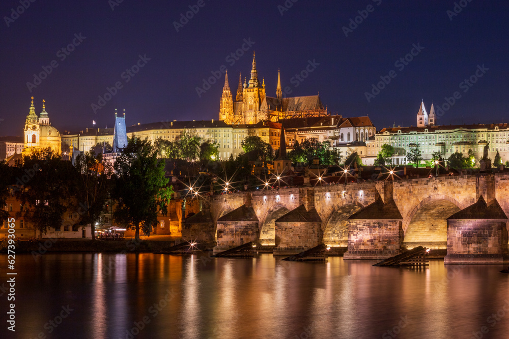 Night time view of Charles Bridge across the Vltava River in Prague with St. Nicholas Church to the left and Prague Castle and St. Vitus Cathedral