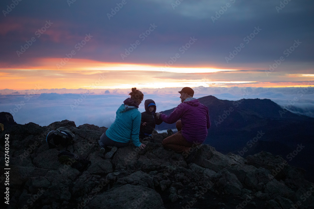 Fototapeta premium Family on a mountain top above the clouds at Haleakala watching the sunrise over the Pacific Coast; Haleakala National Park, Maui, Hawaii, United States of America