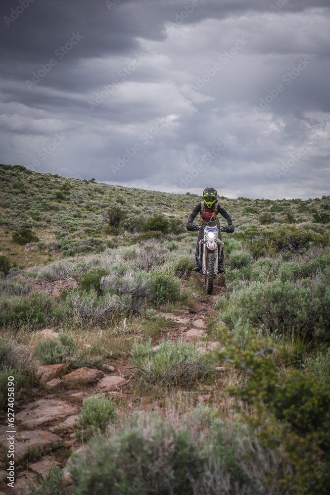 Fototapeta premium Female Dirt biker through sage brush desert terrain with stormy sky back drop near Twin Falls Idaho