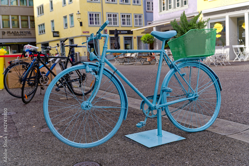 Blue painted bicycle with basked with flowers at the old town of Swiss City of Winterthur on a cloudy spring day. Photo taken May 17th, 2023, Winterthur, Switzerland.