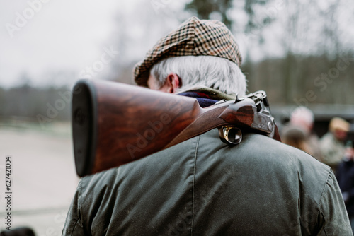 Older man on a hunt. Senior hunter with grey hair, tweed cap and oilskin jacket carrying a shot gun on his shoulder. Pheasant hunting in fall