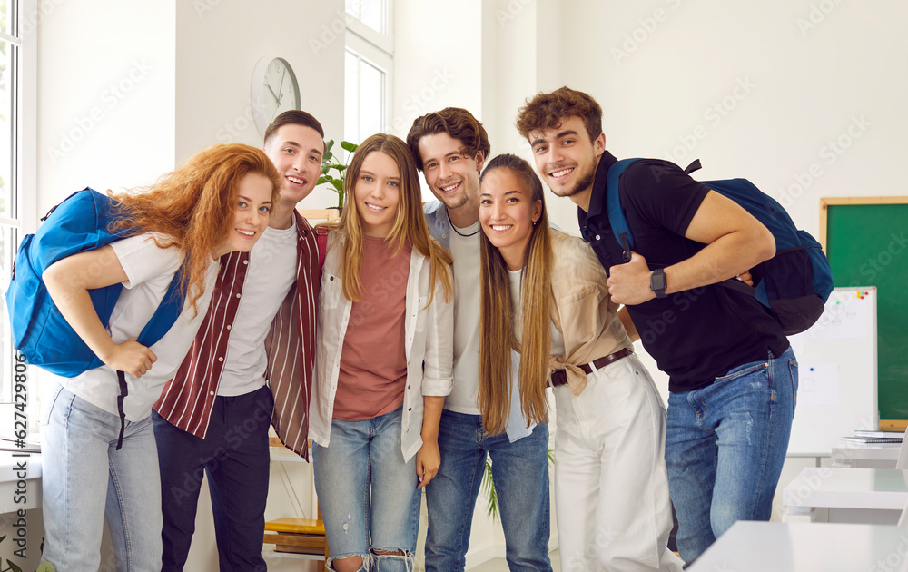 Obraz premium Group portrait of happy diverse school, college or university students and friends in classroom. Several young different multiracial people standing together, hugging, looking at camera and smiling