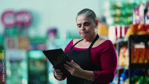 Stressed female entrepreneur owner of small business struggling with hard times holding tablet and staring at the bottom line of the grocery store