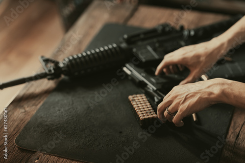 A man is disassembling a gun above the wood table. Black gun, male hands and wooden table underneath.