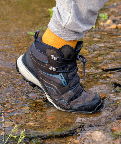 Man wearing outdoor shoes and trekking in a park outdoor by the lake, boots in the lake water