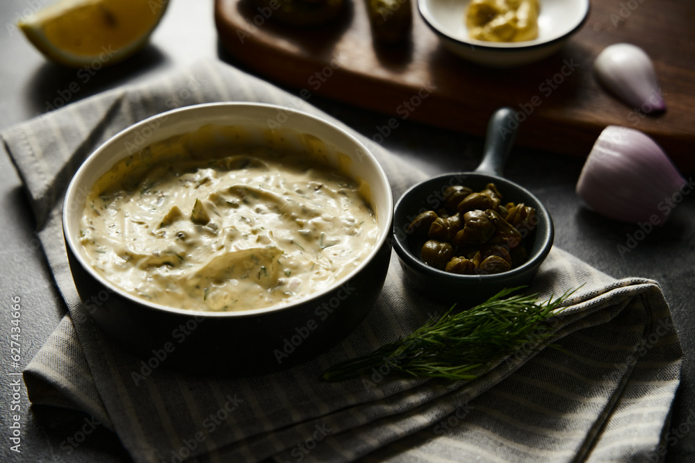Classic Tartar Sauce with it ingredients on dark stone or marble background. Mayonnaise with dill and pickled cucumbers with lemon. Classic Tartar Sauce with it ingredients on dark stone or marble background. Mayonnaise with dill and pickled cucumbers with lemon.