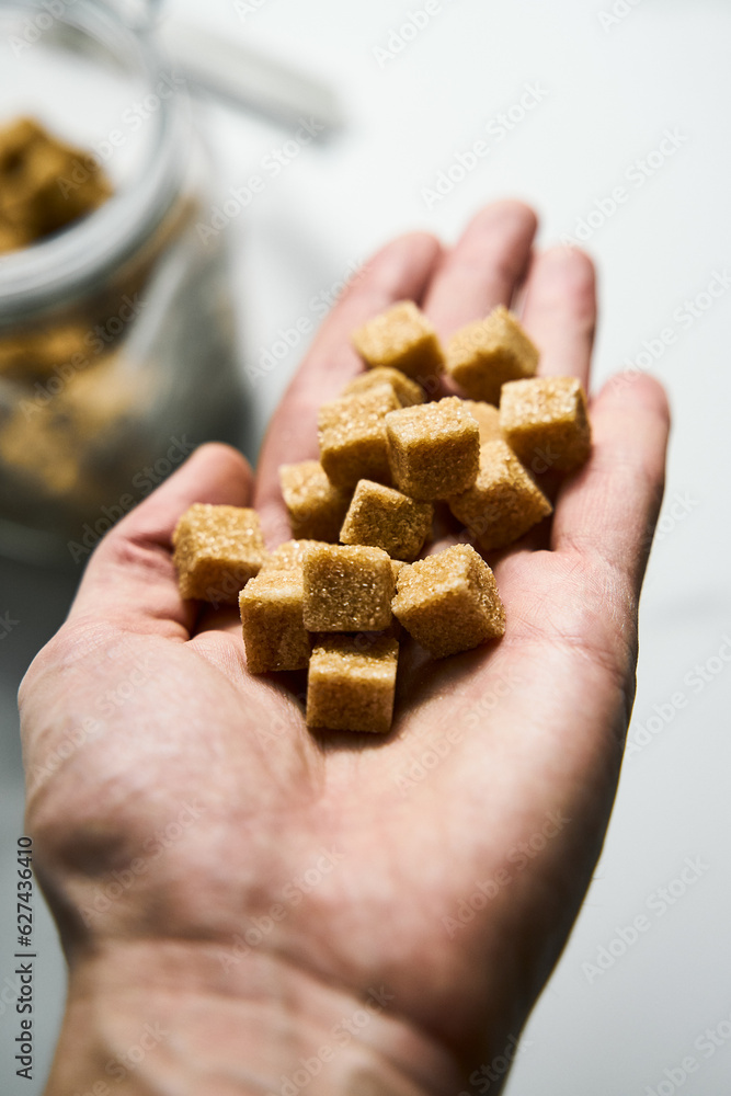 Brown sugar cubes in a man's hand and in the jar on white marble background. Brown sugar cubes in a man's hand and in the jar on white marble background.