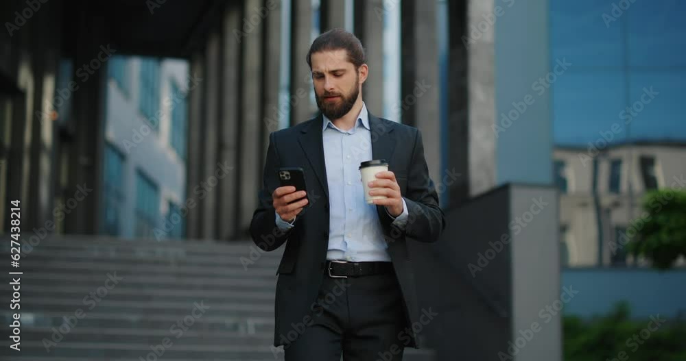 Businessman walking outside office while using smartphone, holding coffee. Businessman walking outside office while using smartphone, holding coffee.