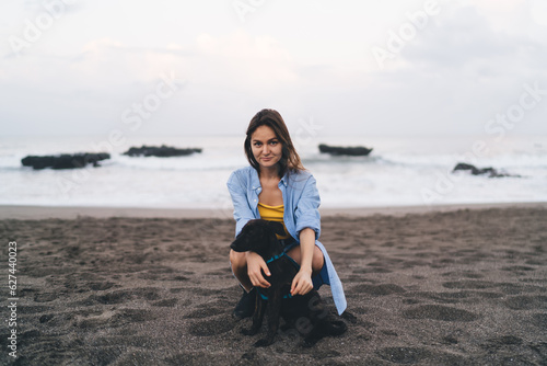 Fototapeta Naklejka Na Ścianę i Meble -  Happy woman sitting on sandy beach with dog