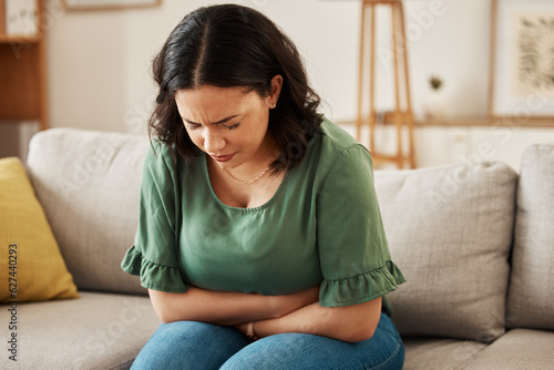 Stress, stomach pain and woman on a sofa with menstruation, gas or constipation, pms or nausea at home. Gut health, anxiety and lady with tummy ache in living room from ibs, bloated or endometriosis photo