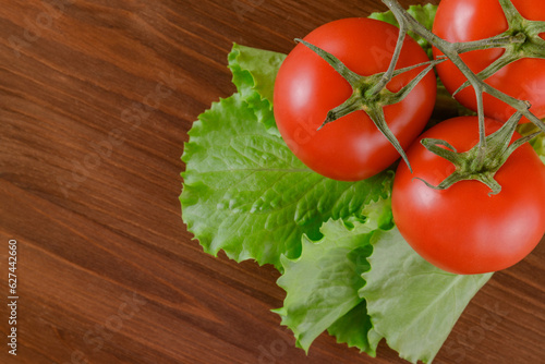 Fresh, ripe red tomatoes and lettuce.  A set of lettuce and tomato branch lie on the wooden table. Closeup. Top view.