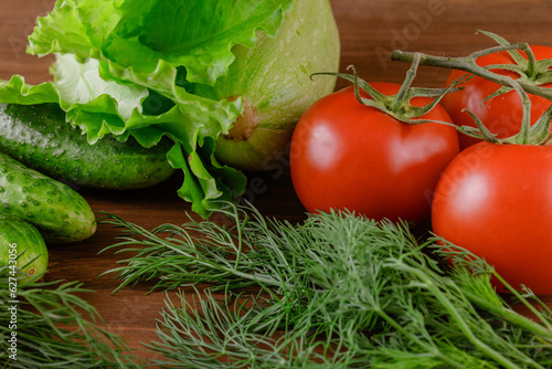 A set of several cucumbers, zucchini, dill, lettuce, tomato branch lie on the wooden table. Fresh raw organic vegetables closeup.