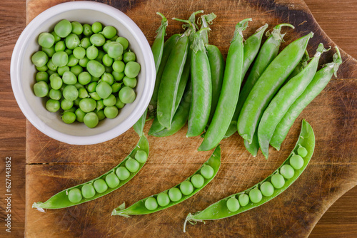 Fresh green pea and pea pods. Pea in bowl and pea pods on wooden board. Top view.