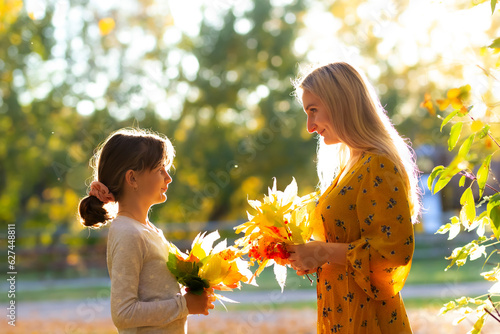 Mom with daughter are holding bouquetes of autumn leaves in the park. photo