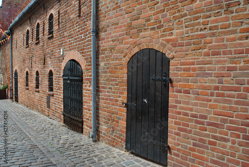 zdjęcie średniowiecznego  ceglanego muu z drzwiami przy kamiennej ulicy