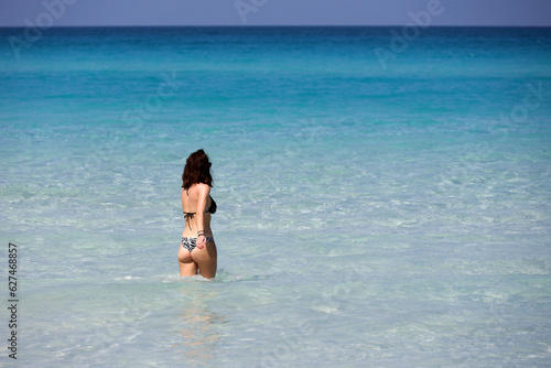 Woman in bikini walking in blue sea water. Beach vacation on Caribbean islands