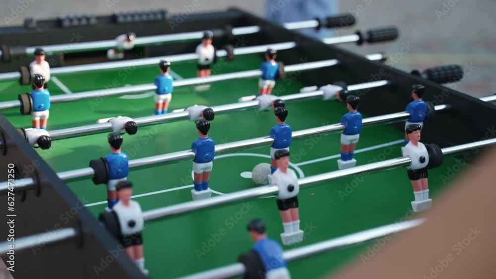 Teenager puts ball on green kicker field to start game and begins to rotate handles with fixed players, close-up. Playing table football in open air and entertainment for holiday guests. Teenager puts ball on green kicker field to start game and begins to rotate handles with fixed players, close-up. Playing table football in open air and entertainment for holiday guests.