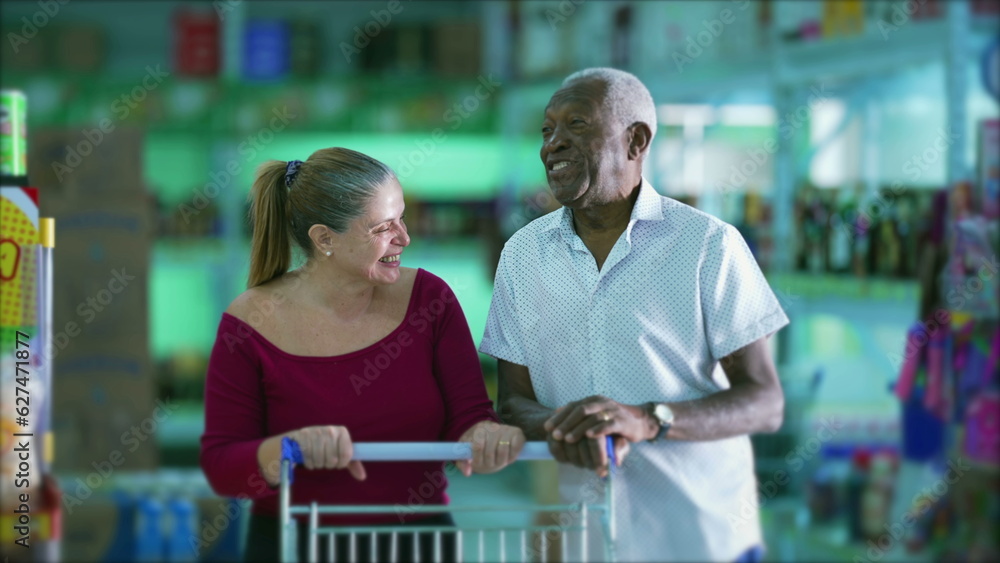 Grocery shoppers laughing and smiling, authentic candid happy middle-aged woman laughs while conversing with a senior black man posing with shopping cart at supermarket