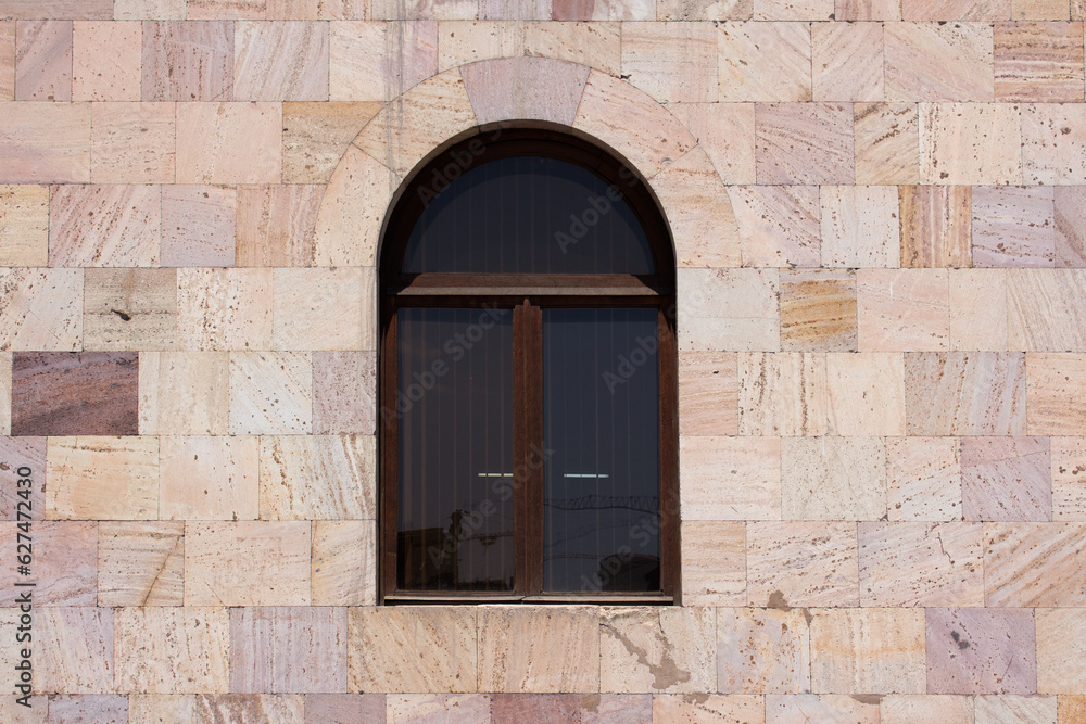Urban frontal minimalistic photo of facade of building. Arched window in pink tuff wall. Stone house in Armenia. Street of Armenian city of Yerevan, concept of architecture, construction. Old house