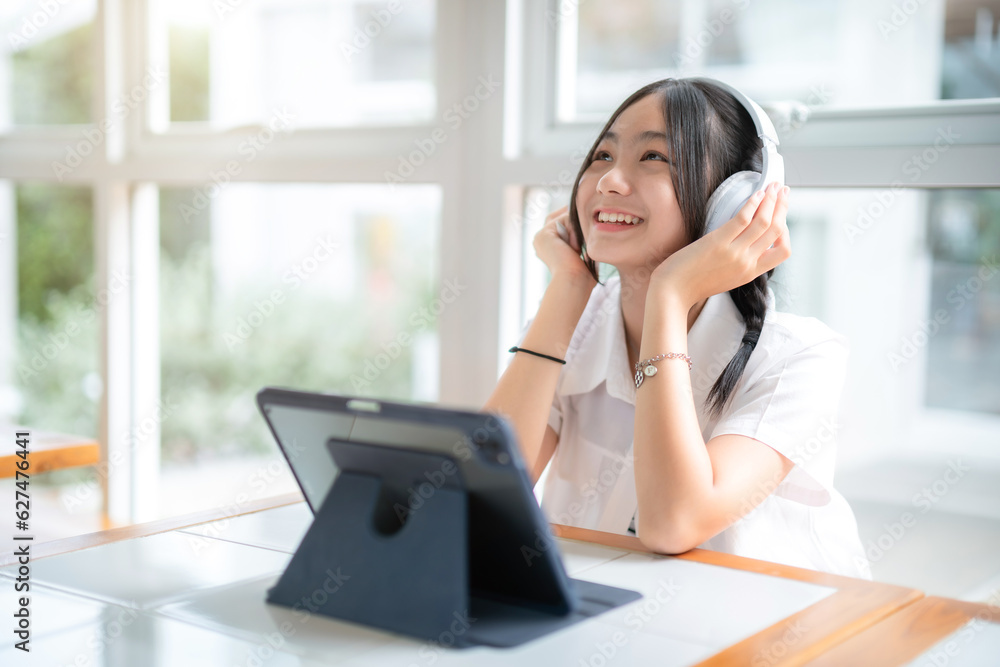 Happy of cute smiles Asian of attractive young Cute girl little wearing headphones and listening music using digital tablet working from at the cafe.Online education, e learning concept. Happy of cute smiles Asian of attractive young Cute girl little wearing headphones and listening music using digital tablet working from at the cafe.Online education, e learning concept.