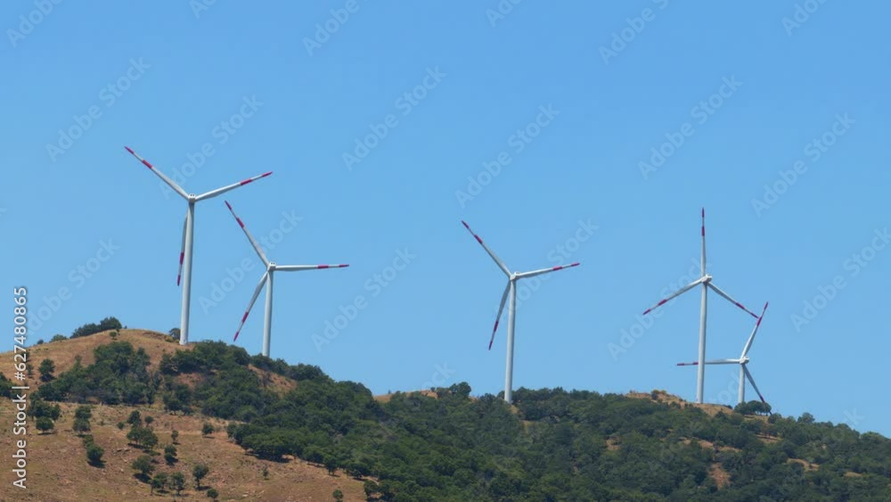 A group of wind turbines turning on a hill, generating green eolic electricity for the electric energy grid A group of wind turbines turning on a hill, generating green eolic electricity for the electric energy grid