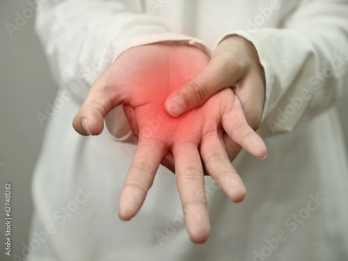Anonymous woman touching her palm, suferring from arthritis disease, close up against grey