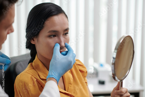 Plastic surgeon letting patient look at her new nose after rhinoplasty