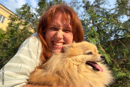 Happy positive young woman holding her Pomeranian Spitz at hands, smile and looking at camera 