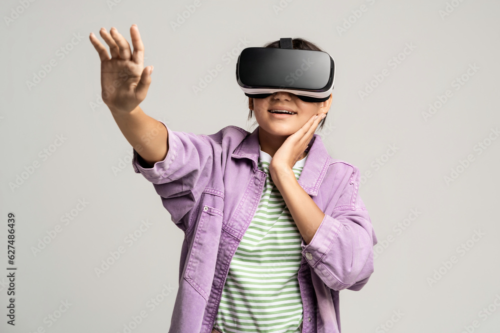 Joyful teenage girl using virtual reality glasses and pulls hand forward. Smiling European teen girl wear vr headset, isolated over studio white background. Future technology, metaverse, cyberspace. Joyful teenage girl using virtual reality glasses and pulls hand forward. Smiling European teen girl wear vr headset, isolated over studio white background. Future technology, metaverse, cyberspace.