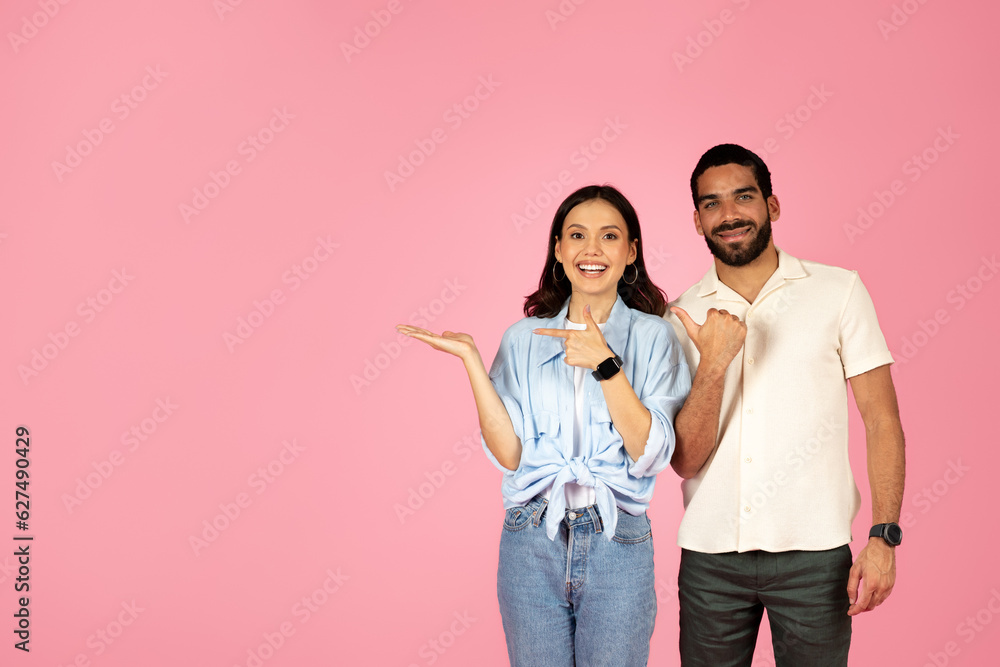 Cute beautiful hispanic couple pointing at copy space on pink Cute beautiful hispanic couple pointing at copy space on pink