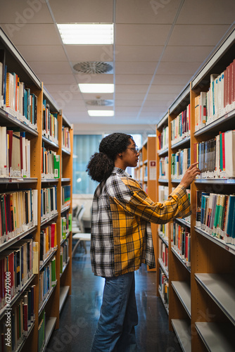 College girl choosing a book to read for an exam. She is at a library.