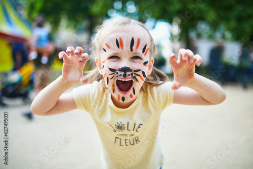 Little preschooler girl with tiger face painting outdoors