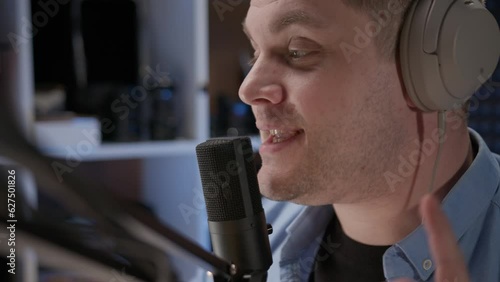 Close up radio host sit in studio and communicates with audience. man in blue shirt and headphones sits in recording studio in front of professional microphone. announcer reads text for video. 