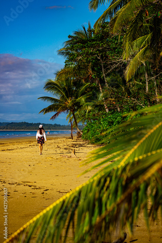 pretty girl walking on the beautiful, tropical beach, enjoying morning sun; mission beach in tropical north queensland, australia; paradise beach with palm trees and tropical plants